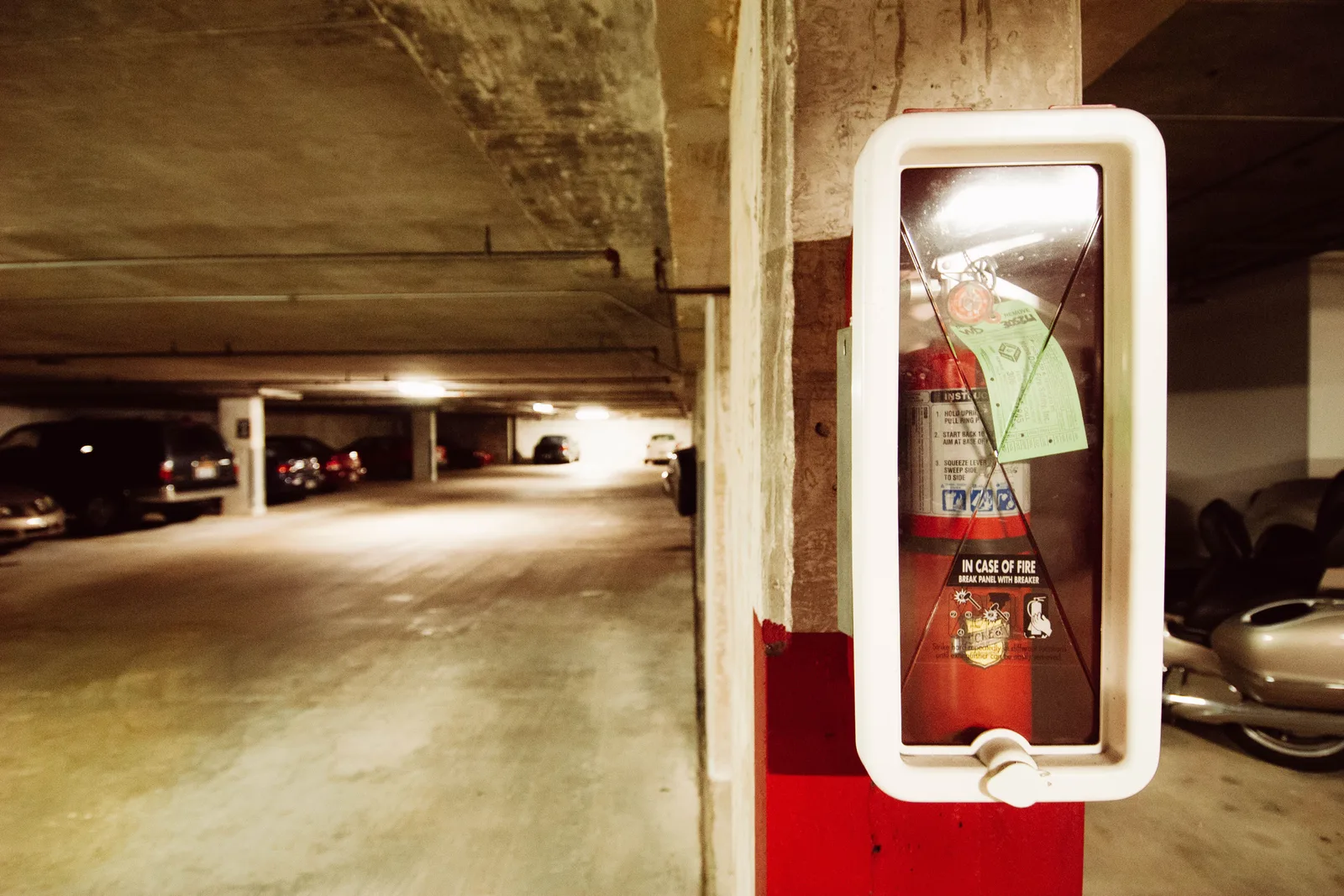 Fire extinguisher in an underground parking garage with parked cars. Apartment EV charger safety response: how teams report issues and decide next steps