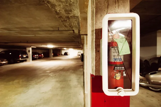 Fire extinguisher in an underground parking garage with parked cars. Apartment EV charger safety response: how teams report issues and decide next steps
