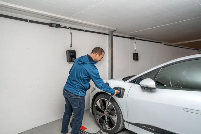 A man connects an electric car to a charging station in a modern indoor garage setting. What to log in an apartment EV charger training record