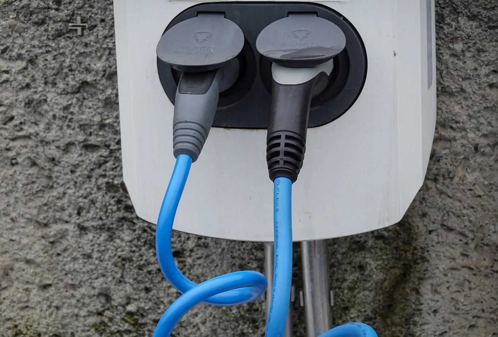 Close-up of an electric vehicle charging station with two cables in sockets against a textured wall. Apartment Level 2 charger care checklist: observe and route