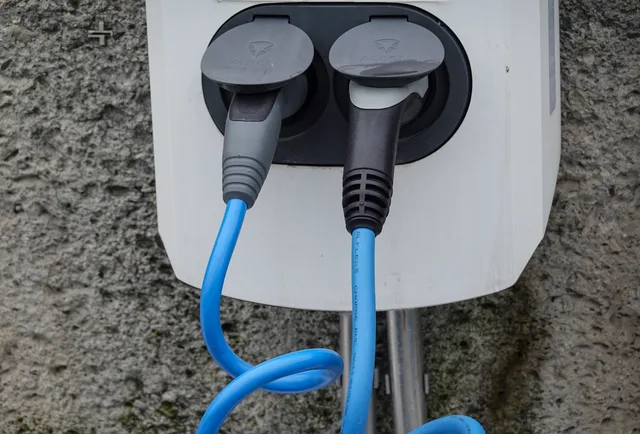 Close-up of an electric vehicle charging station with two cables in sockets against a textured wall. Apartment Level 2 charger care checklist: observe and route