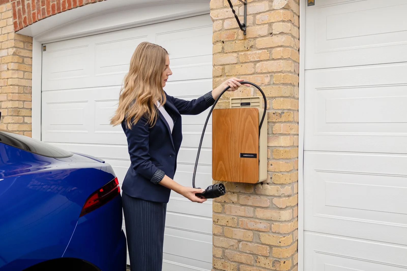 A woman using a home electric vehicle charger on a brick wall in a garage. Multifamily EV demand charge evidence: packets by recipient