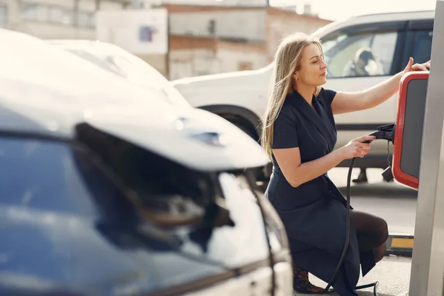 Side view of full length female driver in casual dress squatting near station while charging electric automobile for continuation of driving. How to keep apartment EV charging subscription records ready for a provider change